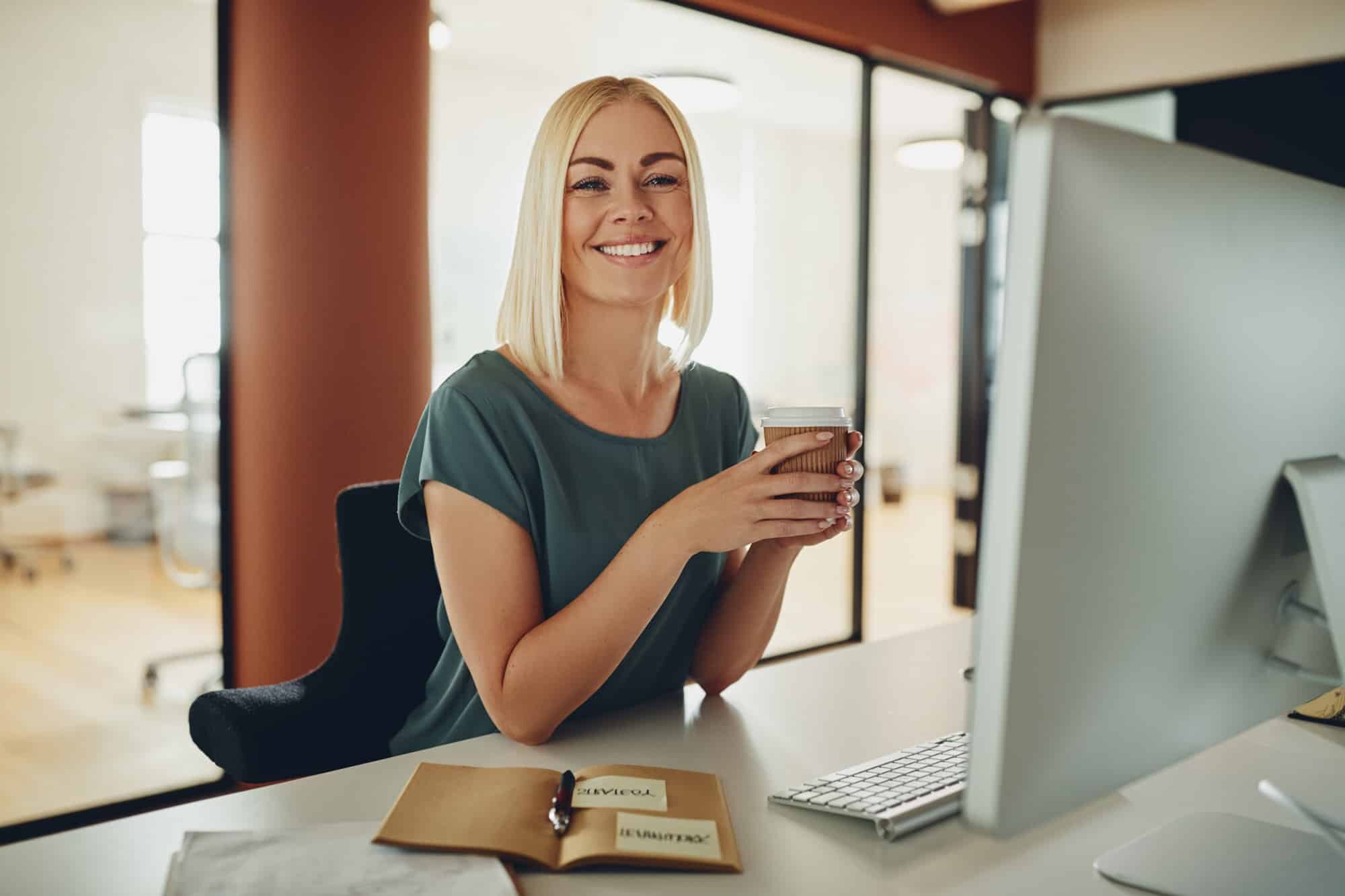 Woman Smiling and drinking coffee in front of computer.
